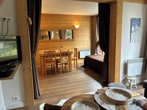 Ein gemütliches Zimmer mit Holzboden, einem Essbereich mit Tisch und Stühlen, einem Bett und einem Fernseher an der Wand.