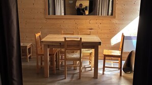 Interior de madeira com mesa e cadeiras, uma janela pequena e um espelho na parede.