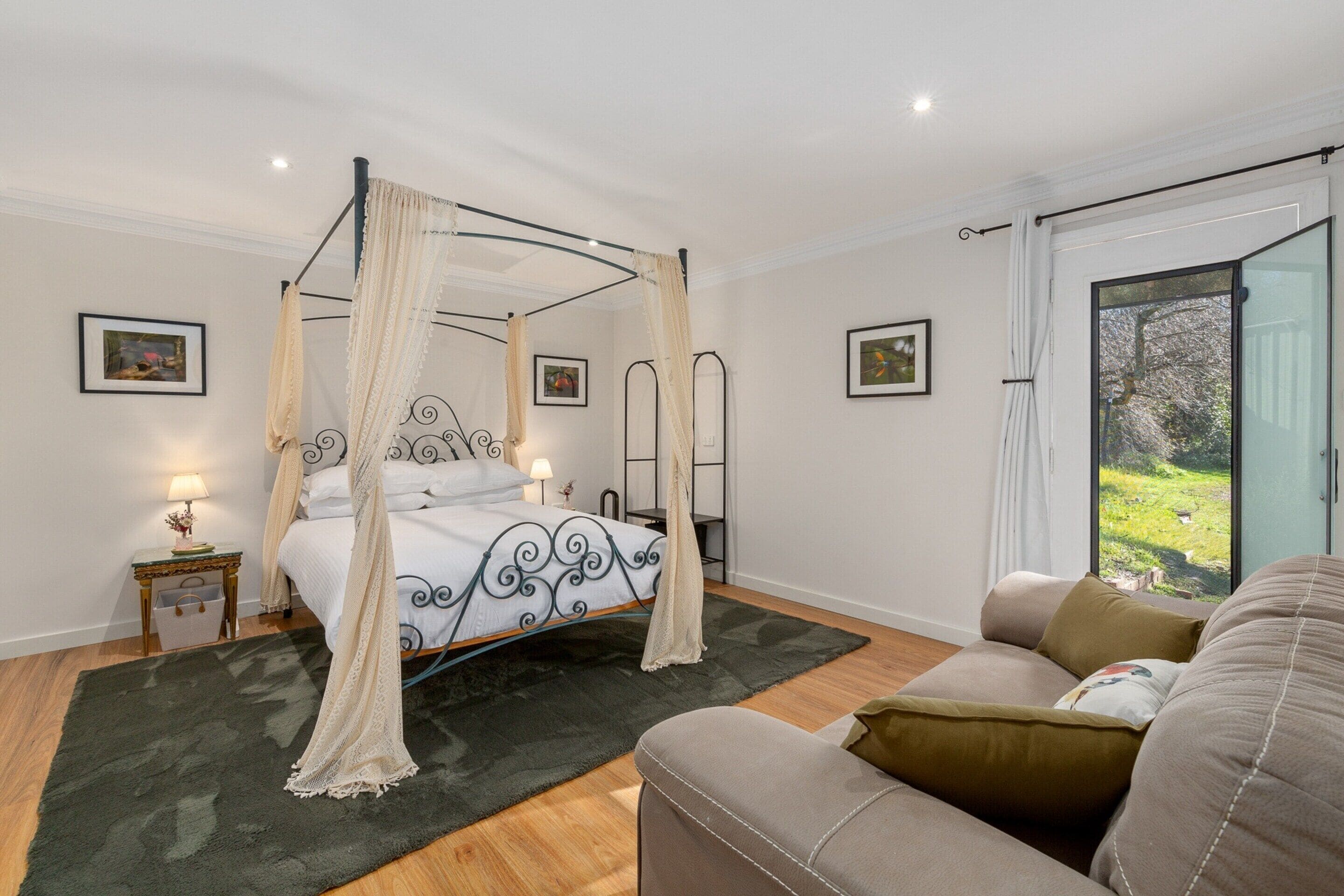 A four-poster bed with a canopy, a sofa, a small table with a lamp, and a picture frame on the wall.
