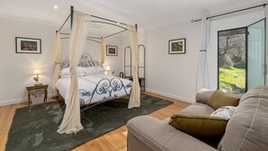 Ein Bett mit Baldachin, eine Sitzecke, ein kleiner Tisch mit Lampe und ein Bilderrahmen an der Wand.