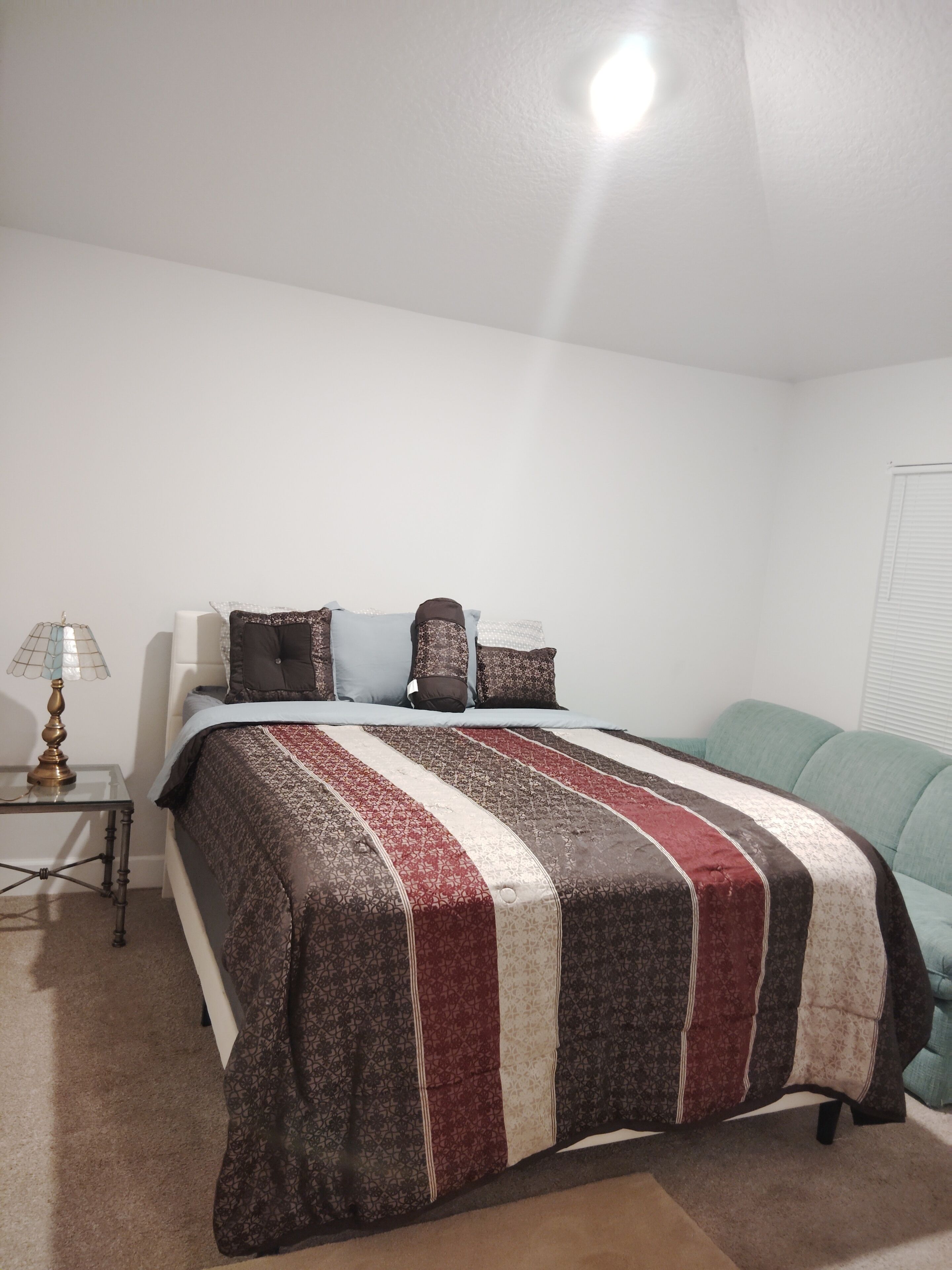 A bedroom with a bed, a nightstand, a lamp, and a window with blinds.