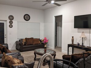 Ein Wohnzimmer mit einer Couch, Sesseln, einem Couchtisch, einem Fernseher und einem Deckenventilator.