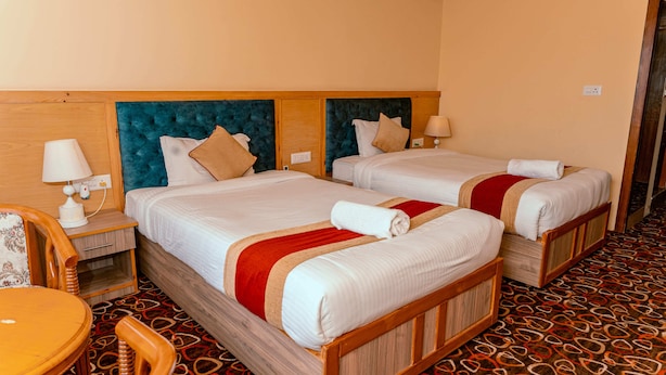 A hotel room with two beds, wooden headboards, a patterned carpet, and a small table with a chair. - Landmark Diamond Hill (Panaoti)