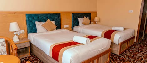 A hotel room with two beds, wooden headboards, a patterned carpet, and a small table with a chair.