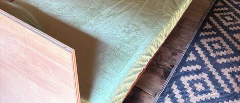 Ein kleiner, rustikaler Raum mit einem Bett, einem Schrank und einem Regal mit diversen Gegenständen.