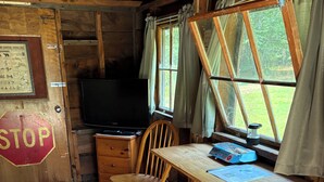 Ein Ferienhaus-Interieur mit einem Holztisch, zwei Stühlen, einem Fernseher und einem Fenster mit Vorhängen.
