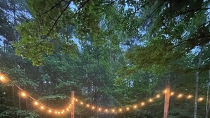 Ein Garten mit Feuerstelle, Holzstühlen und Lichterketten.