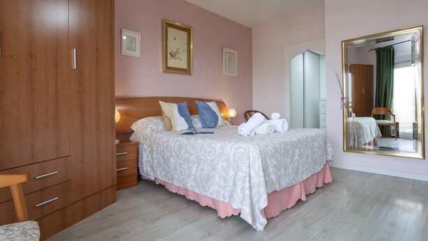 Un dormitorio con un armario de madera, una cama con ropa de cama estampada, una mesita de noche y un espejo grande.