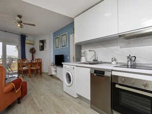 A modern kitchen with a dishwasher, stove, and a dining area with a TV. - Sunstay Flat Duquesa Torremolinos (Torremolinos)