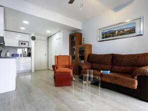 A modern living room with a sofa, armchair, and coffee table, a kitchen area with a microwave, and a dining table. - Sunstay Flat Duquesa Torremolinos (Torremolinos)