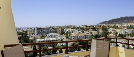A balcony with a table, chairs, and a view of a cityscape with buildings and a mountain.