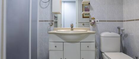 Baño con lavamanos, espejo, inodoro y un cubo de basura.