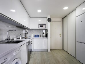 A modern kitchen with a built-in washing machine, a microwave, and a clock on the wall. - Sunstay Flat Duquesa Torremolinos (Torremolinos)