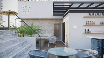 Un espace extérieur moderne aménagé avec une table en verre et des chaises en osier, un mur en pierre et un escalier menant à un niveau supérieur.