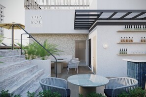 A modern outdoor seating area with a glass table and wicker chairs, a stone wall, and a staircase leading to an upper level.