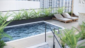 Un área de piscina en la azotea con sillones de descanso y un jacuzzi, rodeada de follaje y arquitectura moderna.