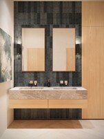 A modern bathroom with a double vanity, dark tiled backsplash, and wooden cabinetry.