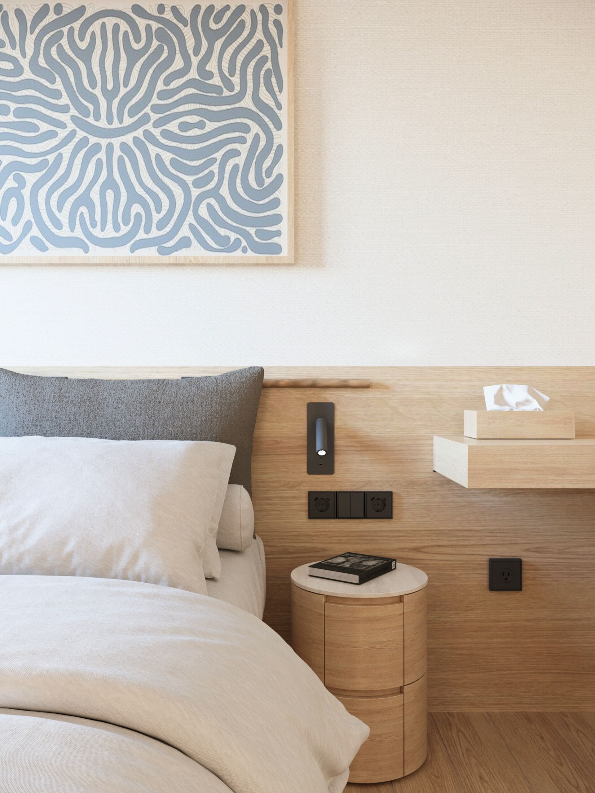 A neatly made bed with a gray pillow, a bedside table with a book, and a wall-mounted shelf with a tissue box.