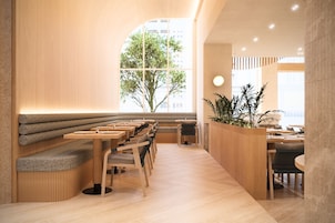 Interior de restaurante moderno com mobiliário de madeira, uma área de estar central e vista para o exterior.