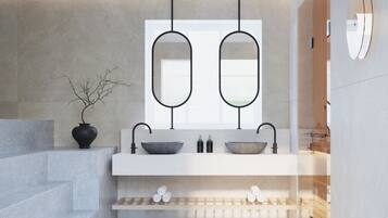 Ein modernes Badezimmer mit einem Doppelwaschbecken, zwei Spiegeln, einer Vase mit Zweigen und einem Handtuchhalter.