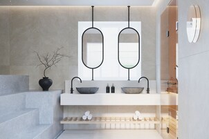 Ein modernes Badezimmer mit einem Doppelwaschbecken, zwei Spiegeln, einer Vase mit Zweigen und einem Handtuchhalter.
