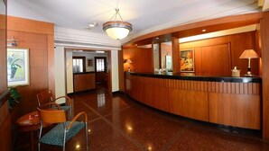 Una hall d'albergo con una reception, sedie, un quadro e un lampadario.