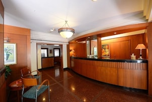 A hotel lobby with a reception desk, chairs, a painting, and a chandelier.