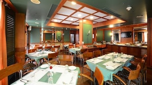 Zona pranzo con diversi tavoli e sedie, angolo cottura e un'ampia finestra.