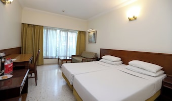 Habitación de hotel con dos camas, un escritorio, una silla y una ventana con cortinas.