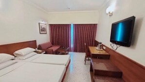 Una camera d'albergo con due letti, una scrivania, una sedia, una televisione e una finestra con tende.