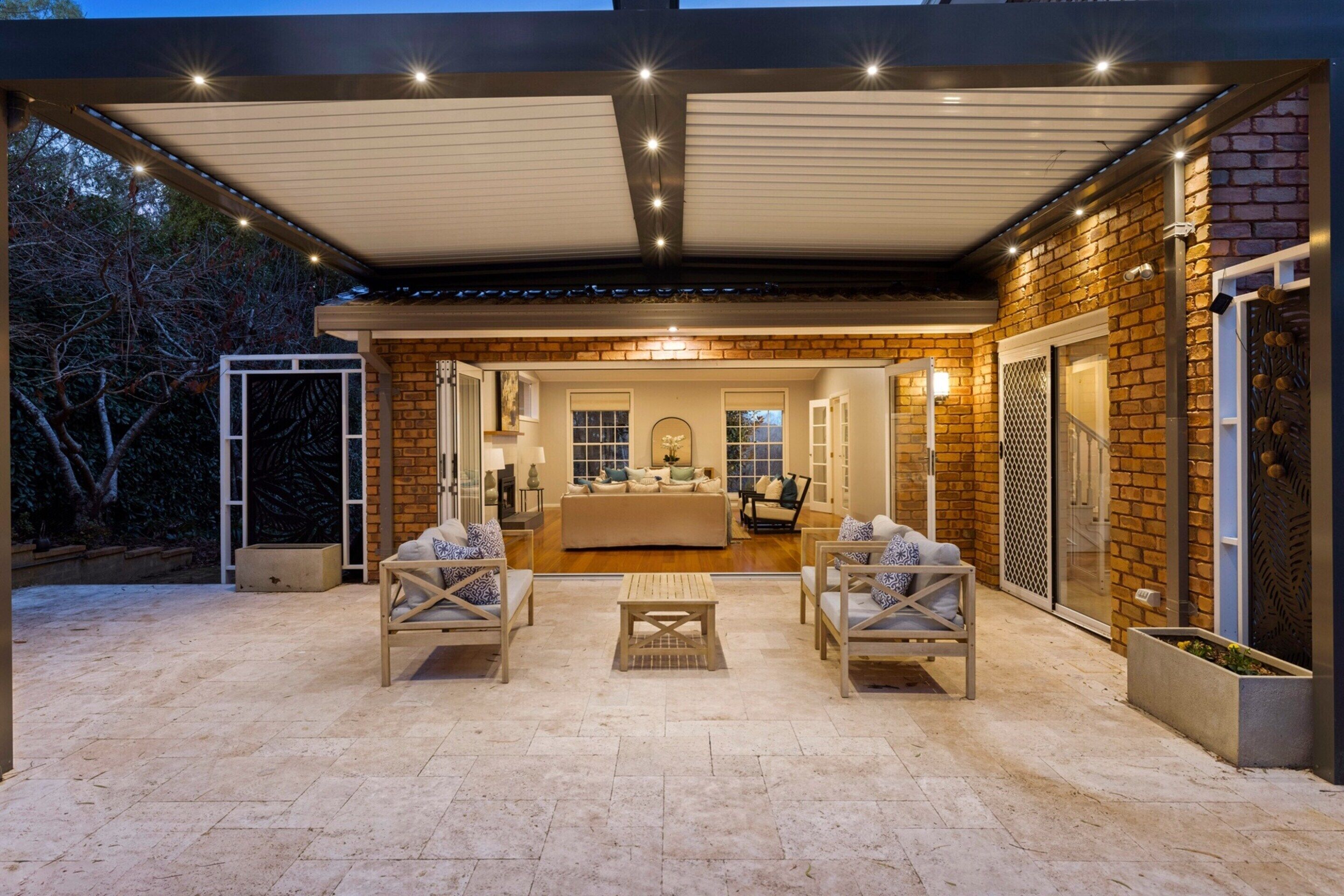 An outdoor patio area with a covered seating arrangement, a kitchen visible through an open door, and a brick exterior wall.