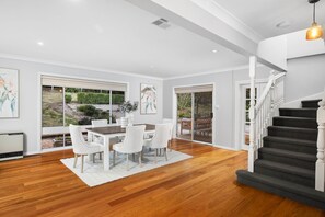 A spacious room with a dining area, a staircase, and large windows. - Carinya Centennial Bowral Spa Retreat (Bowral)