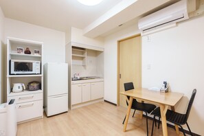 Eine kleine Küche mit Mikrowelle, Kühlschrank und einem Spülbecken. Ein Esstisch mit Stühlen und eine Holztür sind ebenfalls vorhanden.