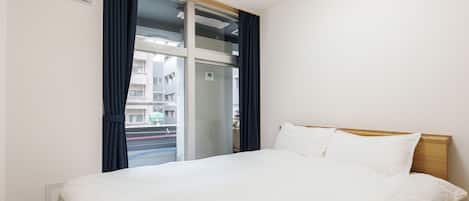 A hotel room with a bed, a window with curtains, and a view of the outside.
