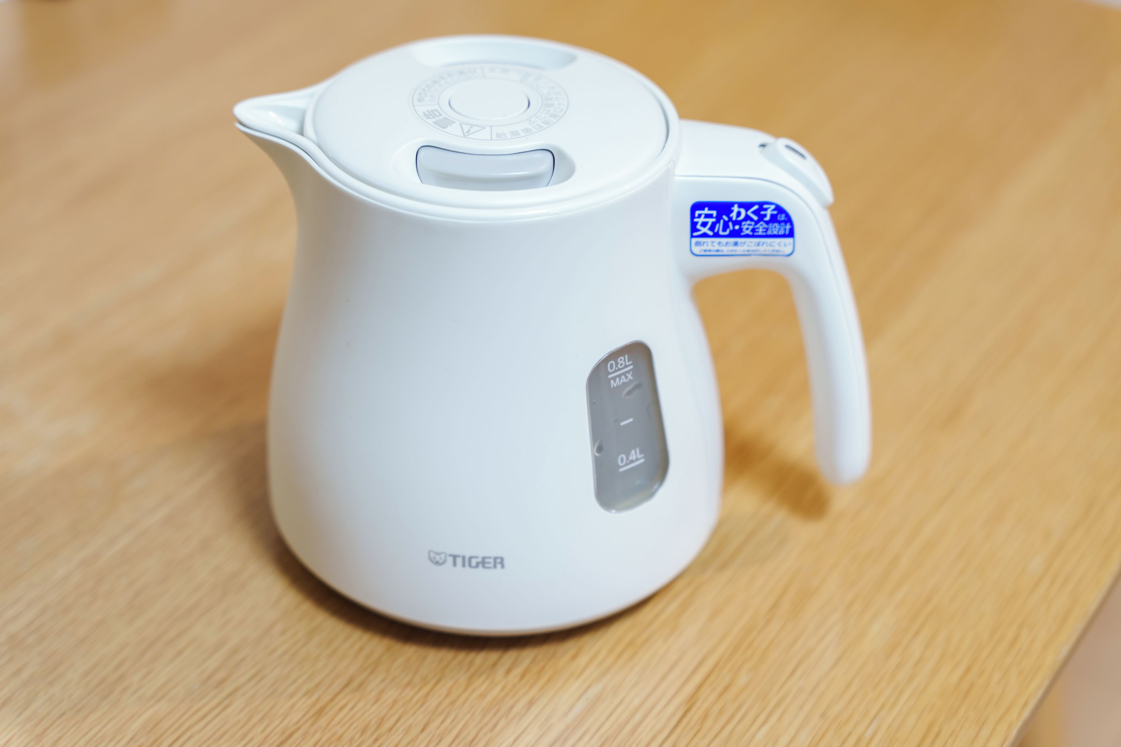 A white electric kettle with a handle and a spout, placed on a wooden surface.