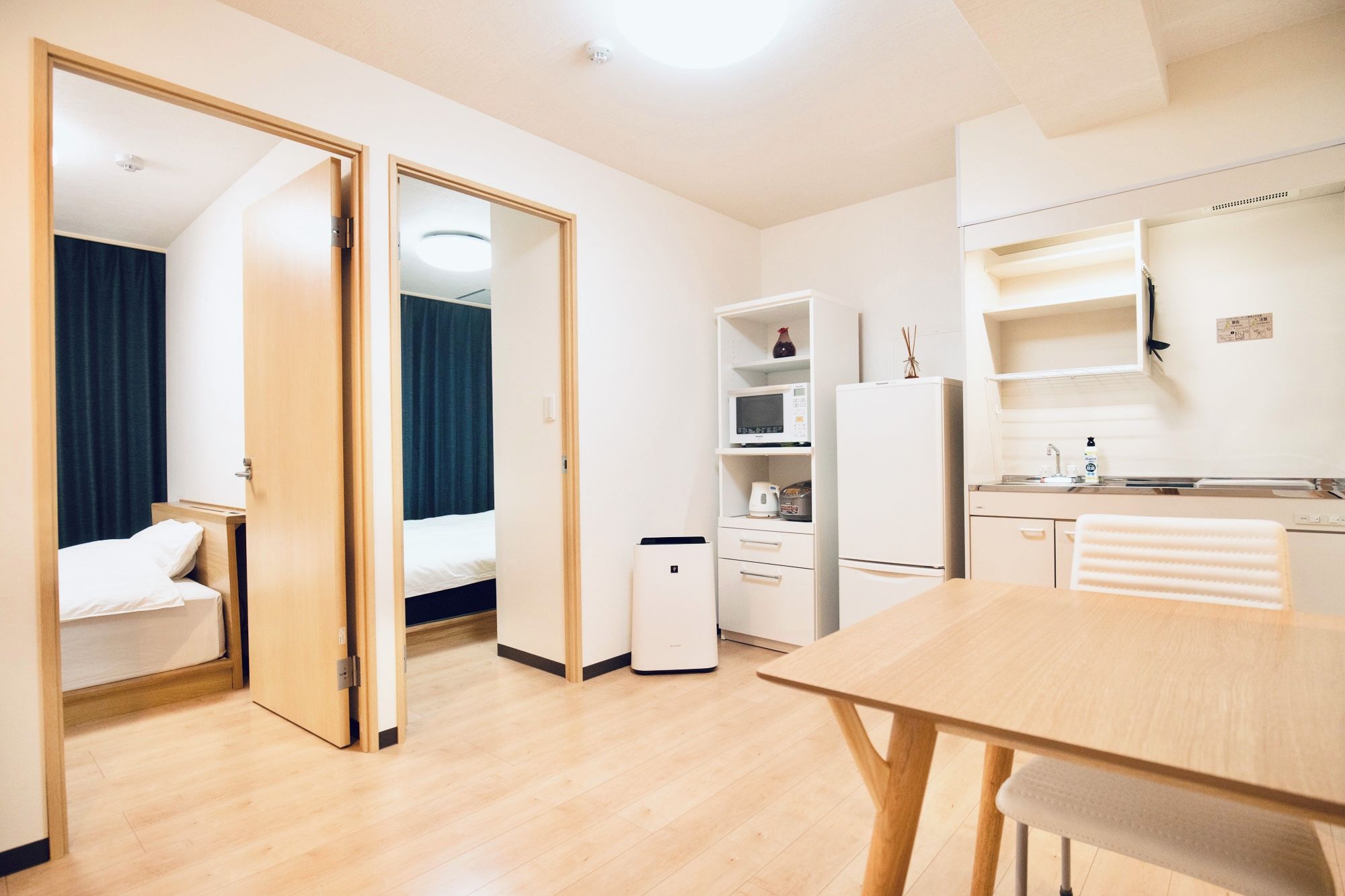 A compact hotel room with a bed, a desk, a kitchenette, and a bathroom.