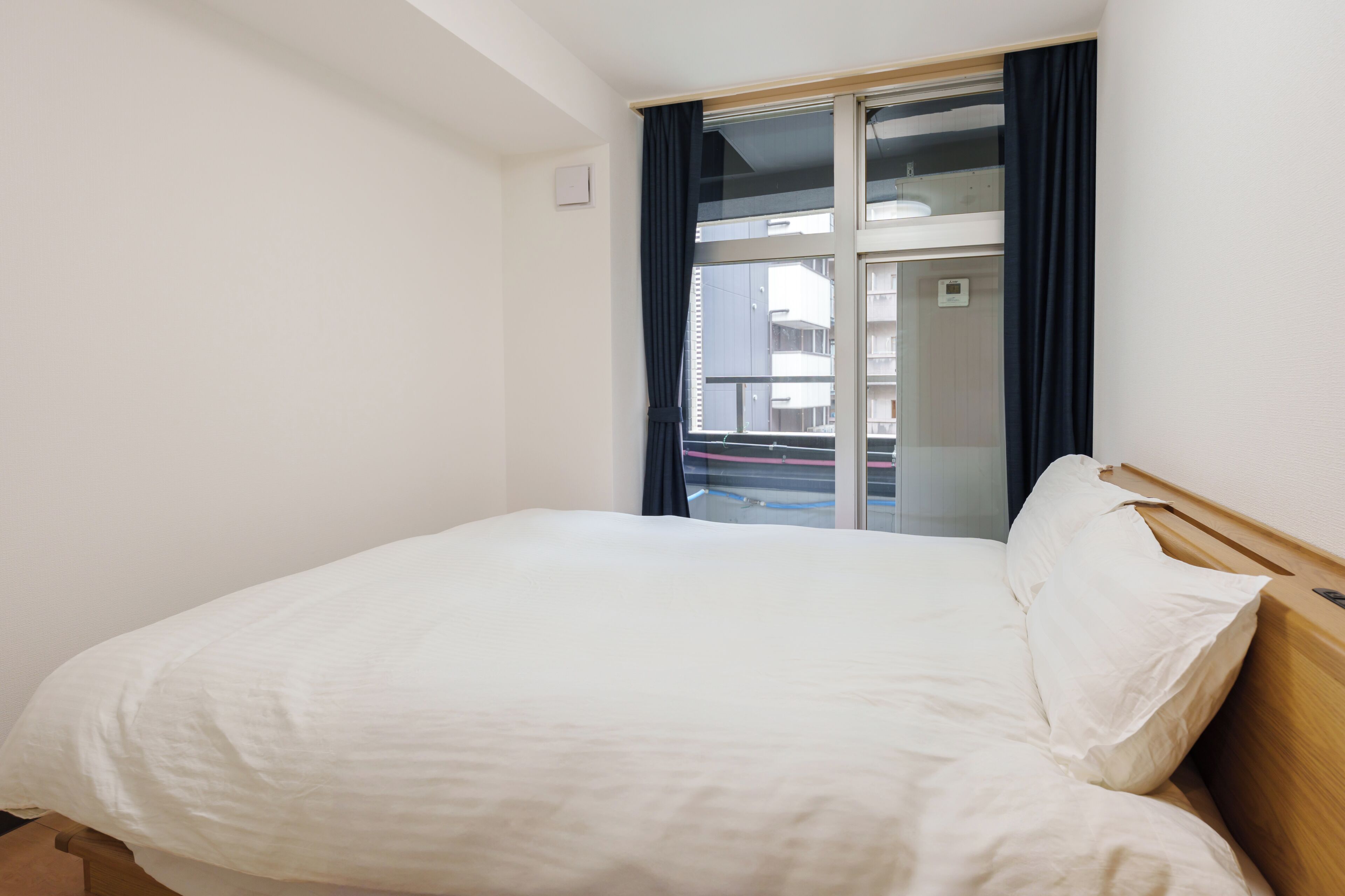 A hotel room with a bed, a window with curtains, and a view of buildings outside.
