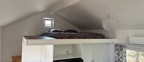 Une chambre avec un lit superposé, une petite fenêtre, un luminaire au plafond et un appareil de climatisation.