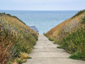 Um caminho de concreto leva a um edifício à beira-mar, rodeado por vegetação gramada.