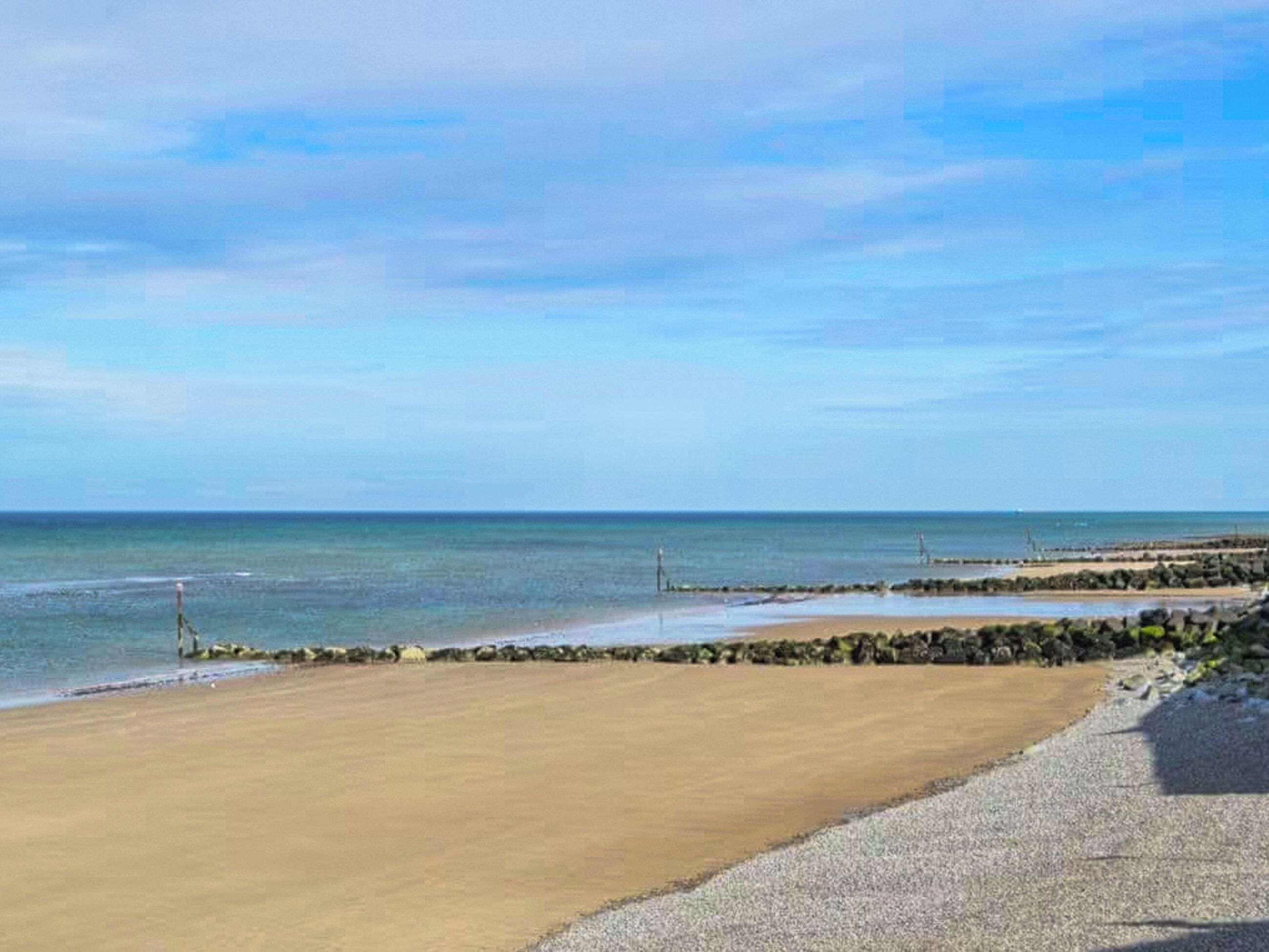 Une plage avec un ciel dégagé, une mer calme et une côte rocheuse.