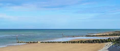 A beach with a clear sky, calm sea, and a rocky shoreline.