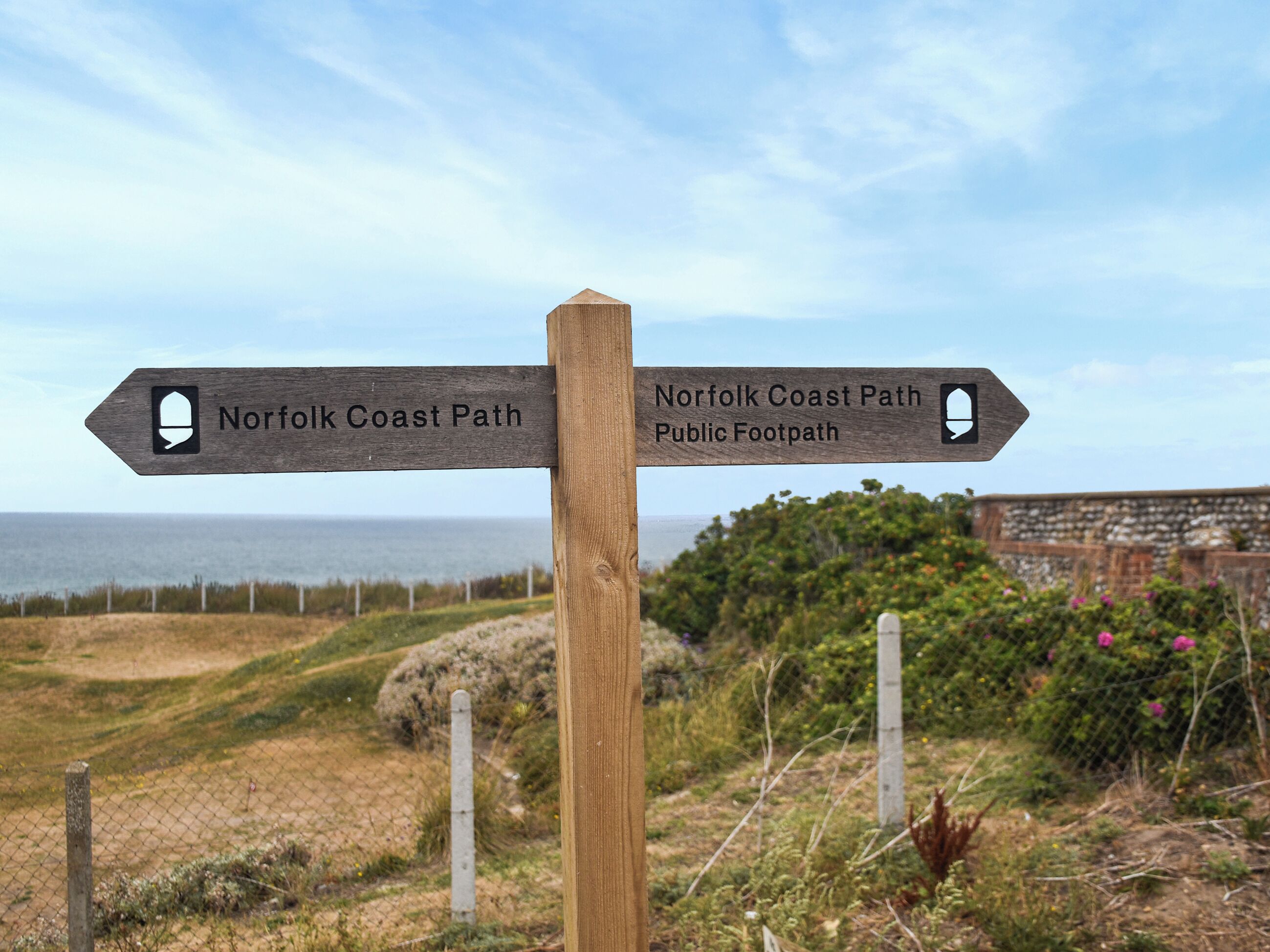 Un senyal de fusta amb dos indicadors de direcció per la ruta de costa de Norfolk i un camí públic.