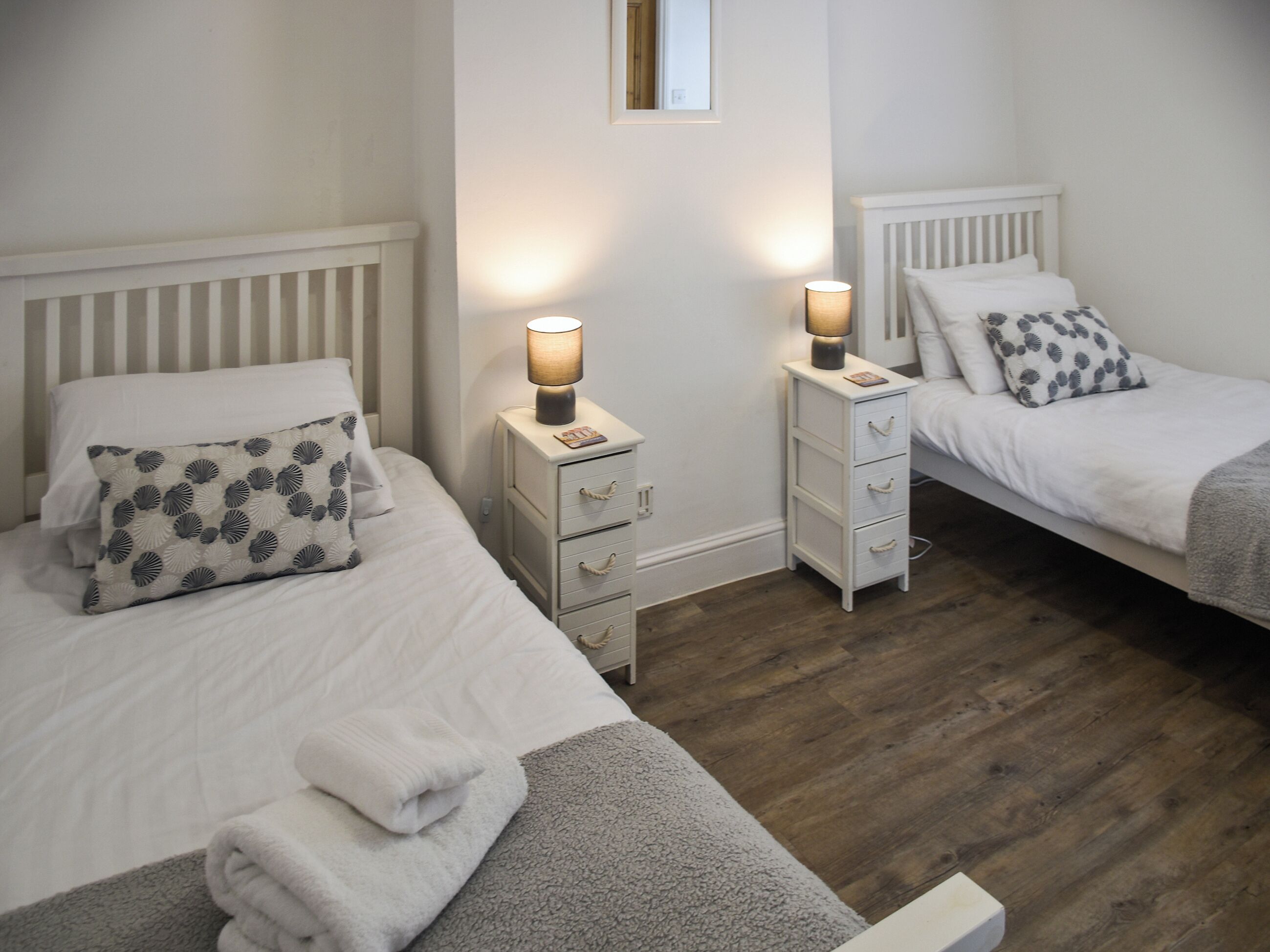 A twin room with two beds, bedside tables with lamps, and a wooden floor.