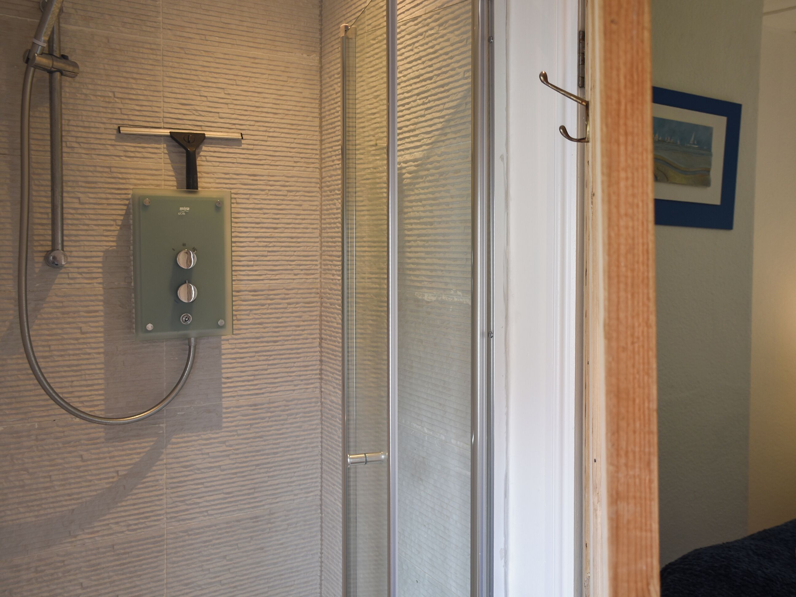 A bathroom with a shower, a control panel, and a door leading to another room.