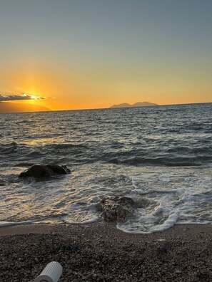 Ein Strand mit Wellen, Kieselsteinen und einem Sonnenuntergang.