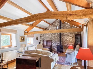 A rustic interior with exposed wooden beams, a stone wall, a fireplace, and a cozy seating area.