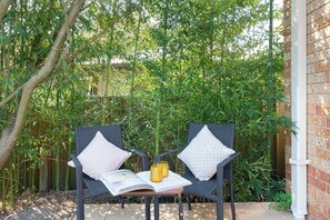 Two wicker chairs with cushions, a table with a book and a glass, and a brick wall. - Prime Location - Walk to Shops & Easy Transport (North Rocks)