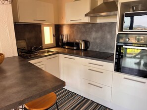 A modern kitchen with white cabinets, a stainless steel range hood, and a built-in oven. - La Croix Holidays (La Croix-Valmer)