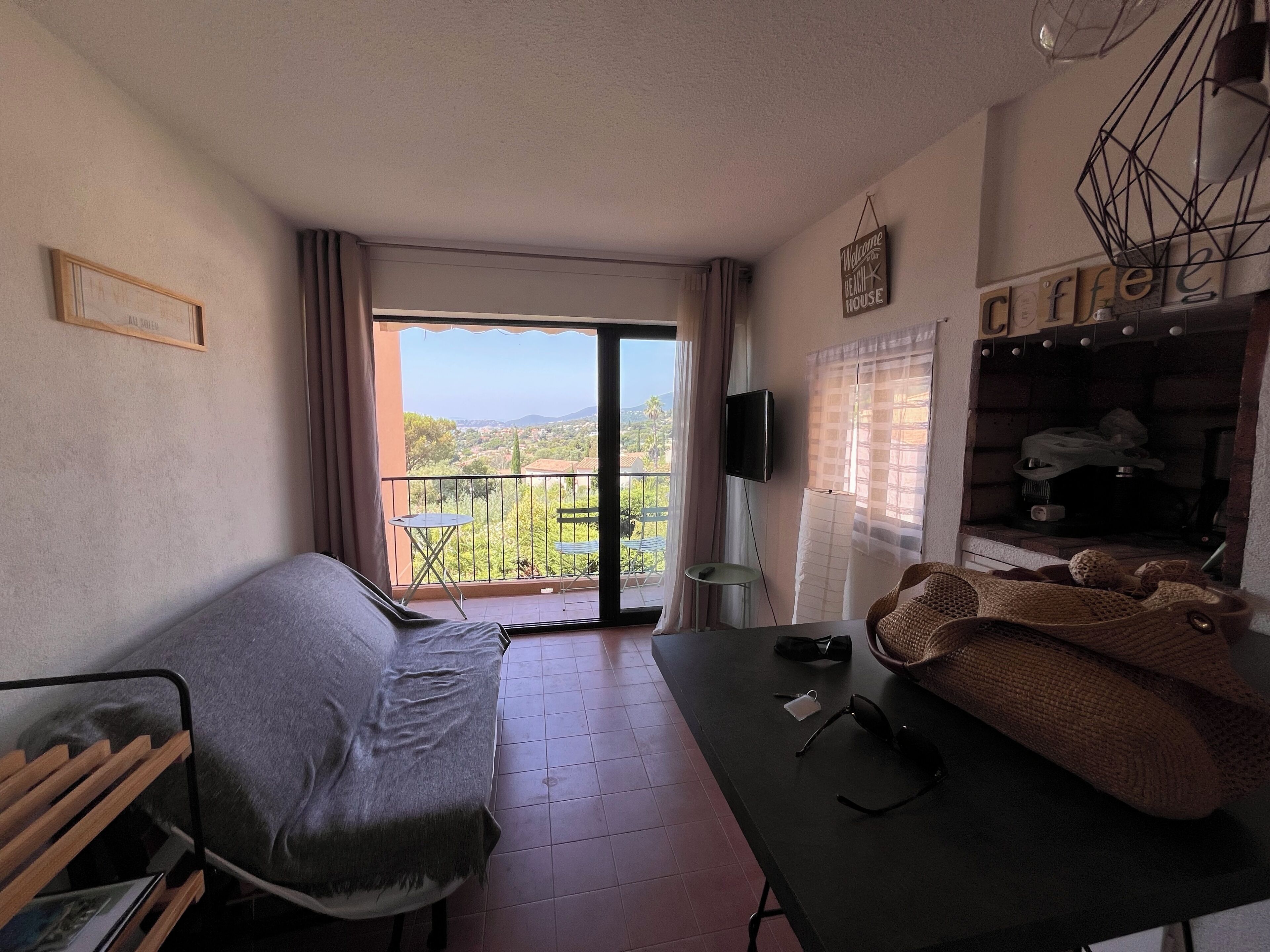 A room with a sofa, a table with sunglasses and a cup, a TV, and a balcony with a view.