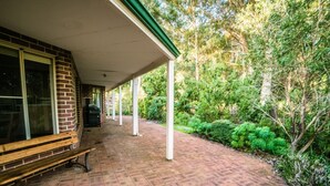 A covered patio area with a brick floor, a bench, and a grill. - Whispering Karri Retreat | 5-Acre Hideaway (Shadforth)